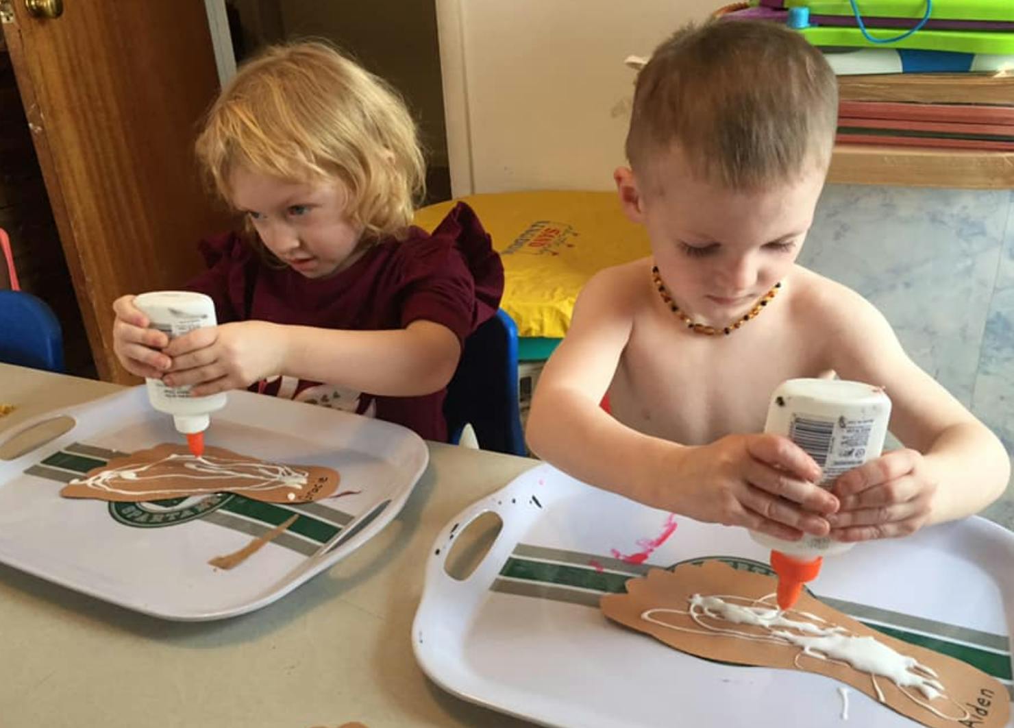 Two children applying glue to craft projects on trays