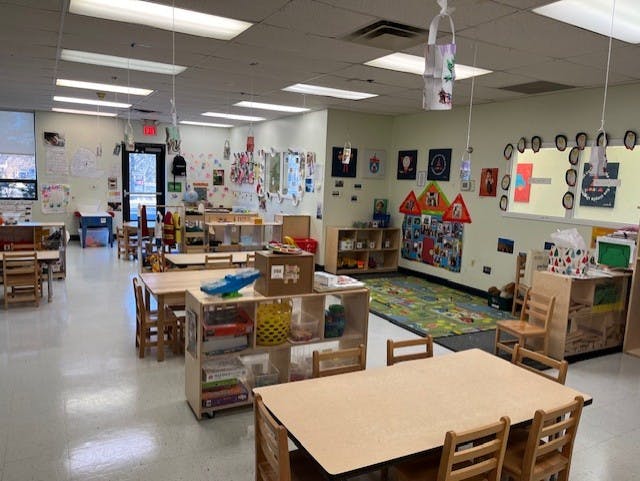 Empty classroom with small tables and chairs, shelves with toys, and artwork on walls