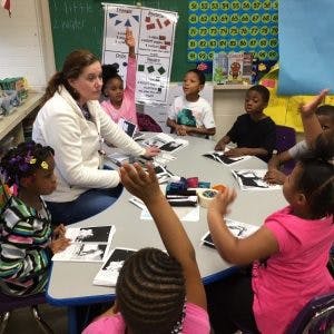 Adult and children sitting at a table with some children raising hands