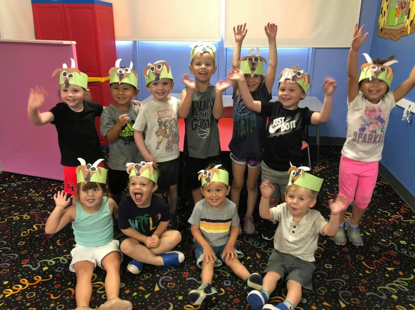 Group of children wearing paper crowns with owl faces, some waving