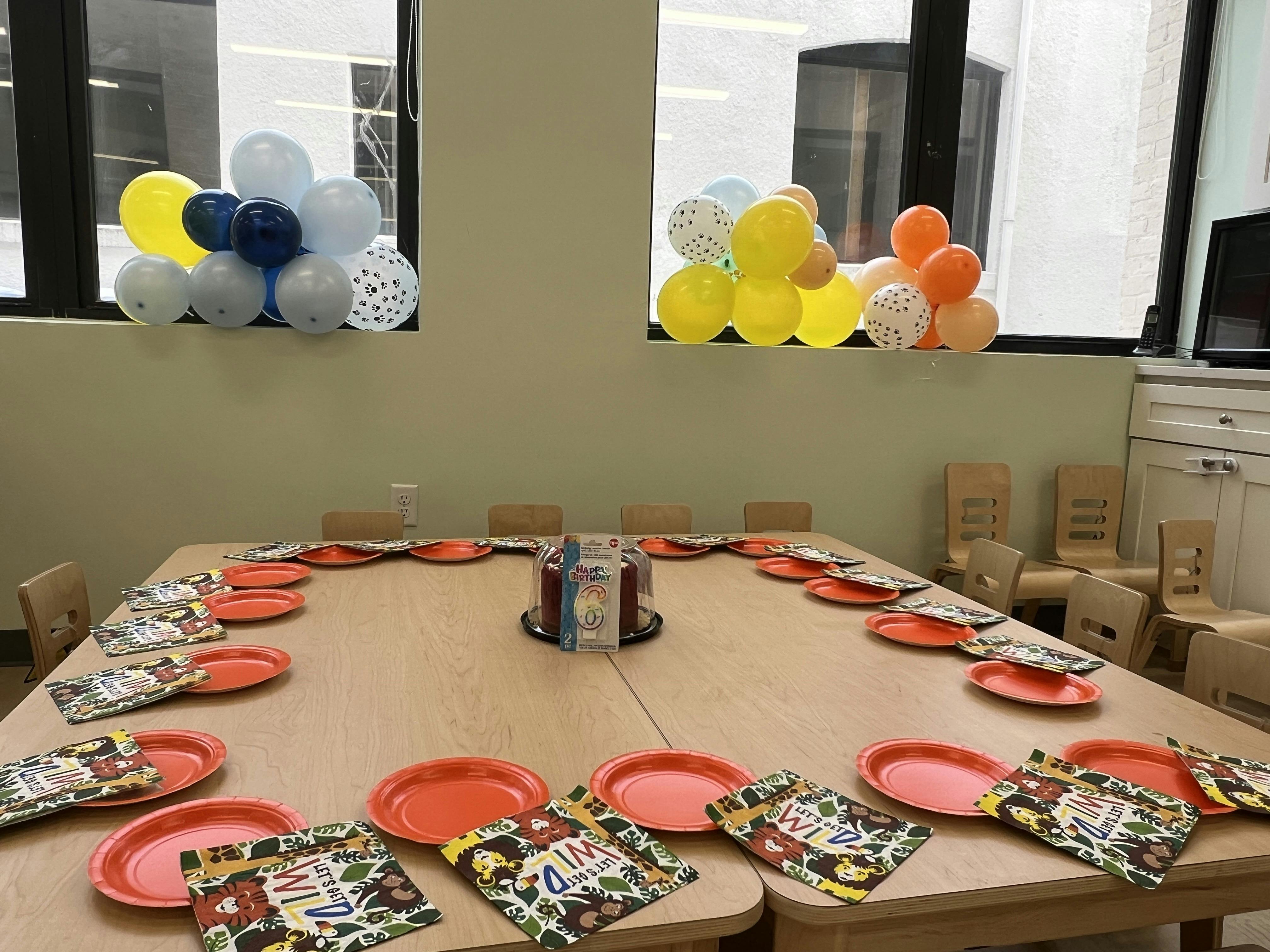 Table set with orange plates and napkins, balloons on windowsills