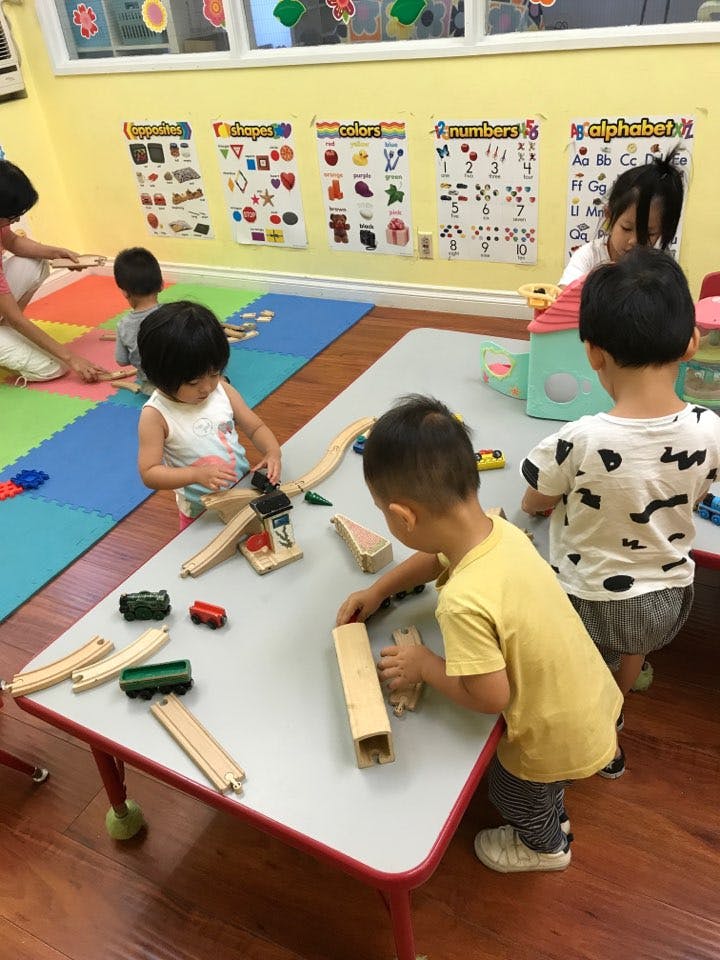 Children playing with wooden train sets and blocks in a classroom