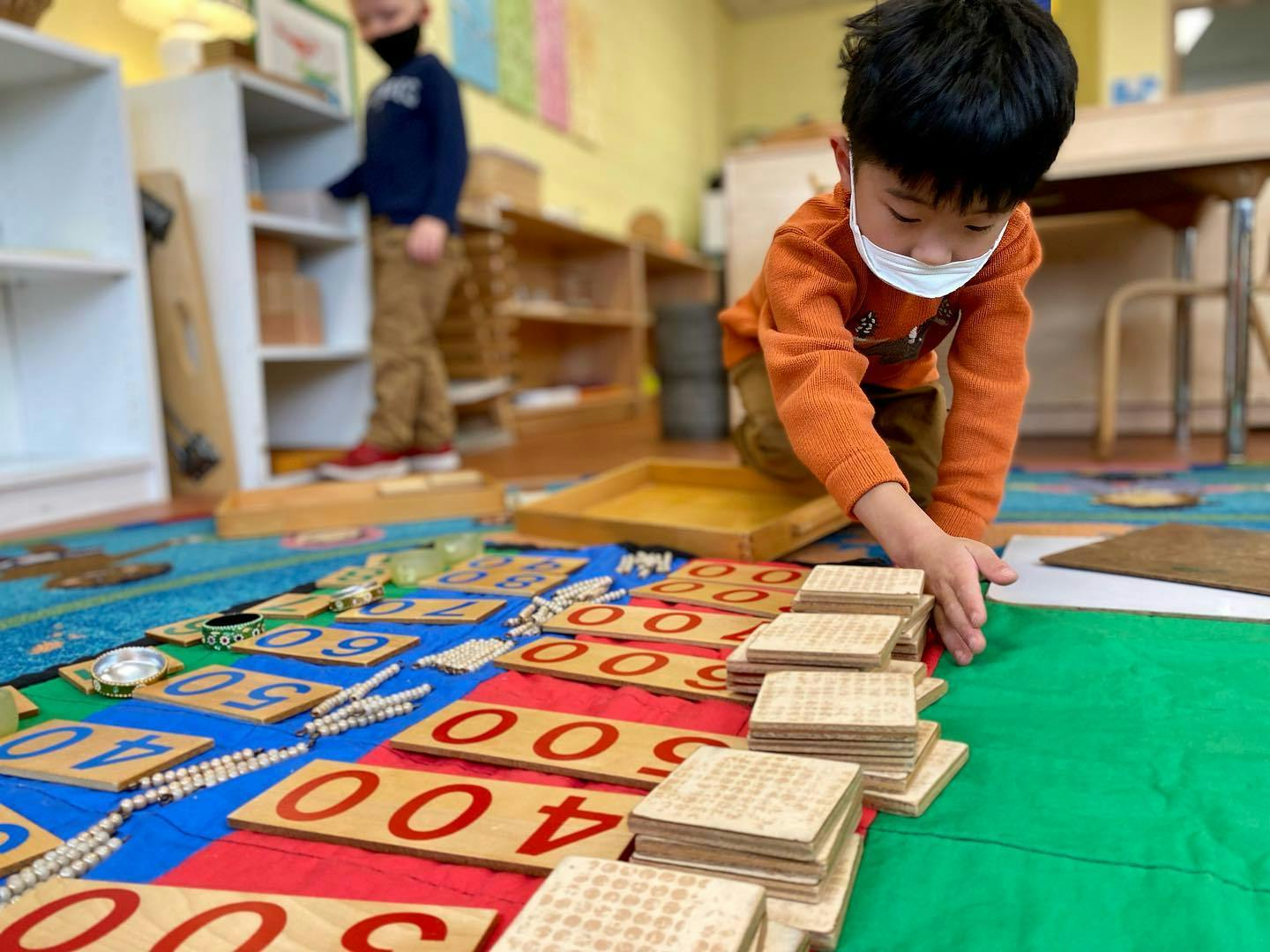 Child in a mask playing with number blocks on the floor