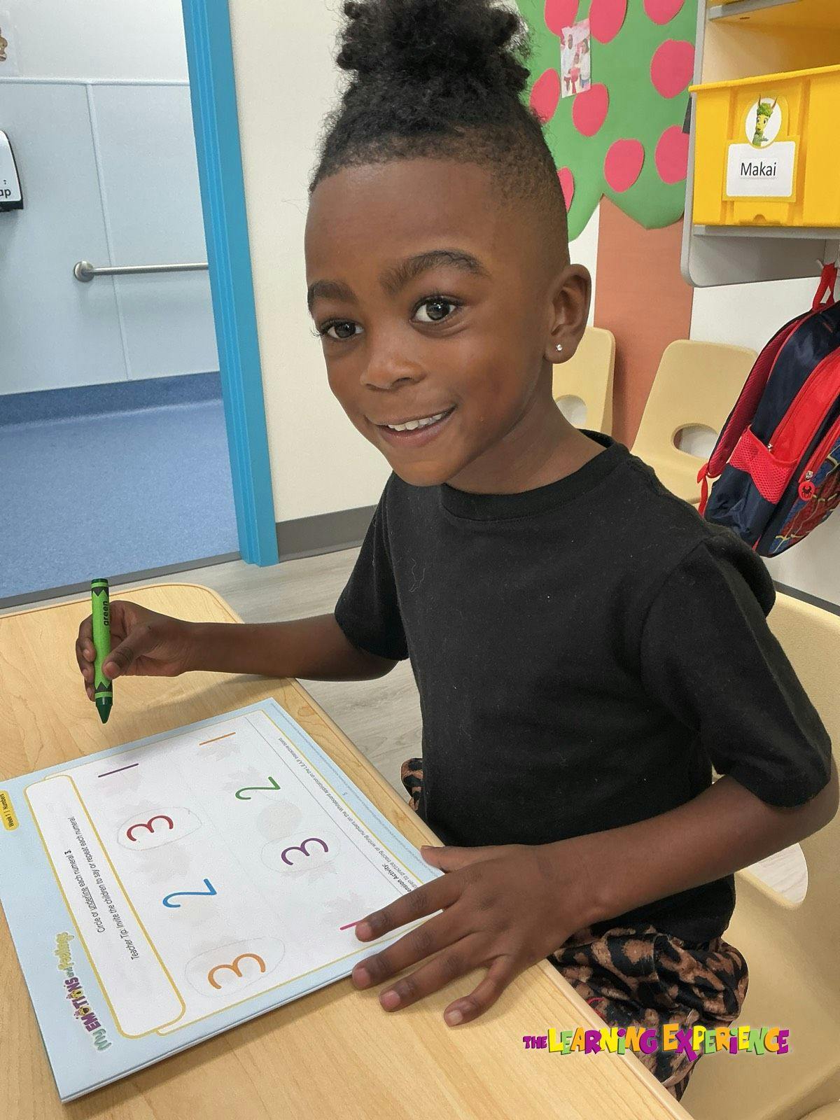 Child sitting at a desk with a crayon and a number tracing worksheet