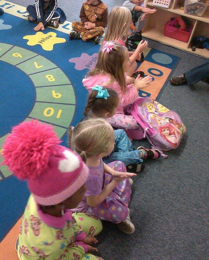 Children sitting on a colorful rug with numbers and shapes in a classroom