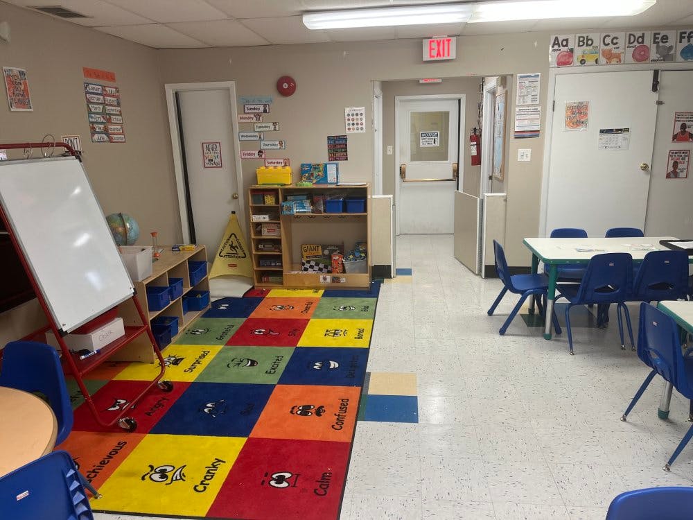 Classroom with child-sized tables and chairs, a whiteboard, and a colorful rug