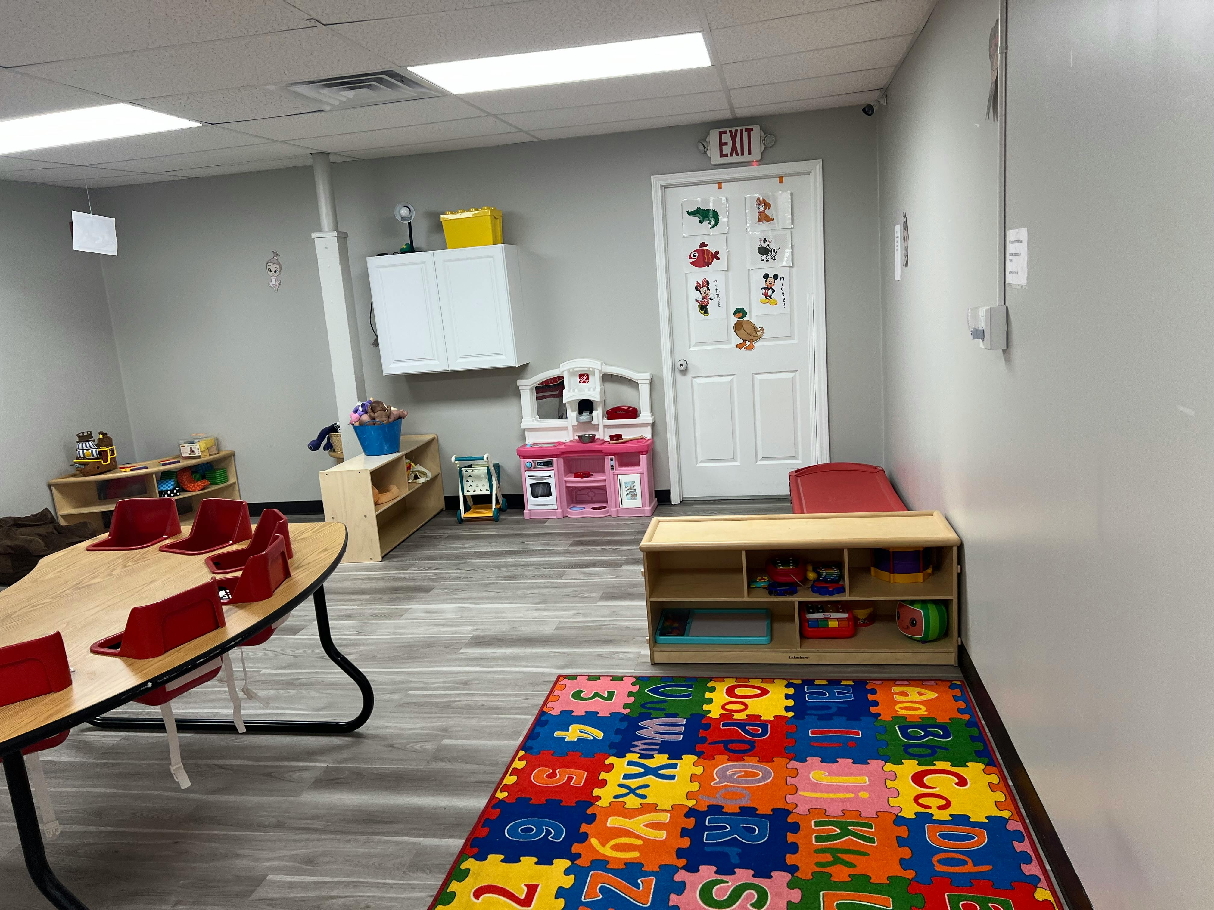 Playroom with a table, chairs, toy kitchen, and alphabet mat