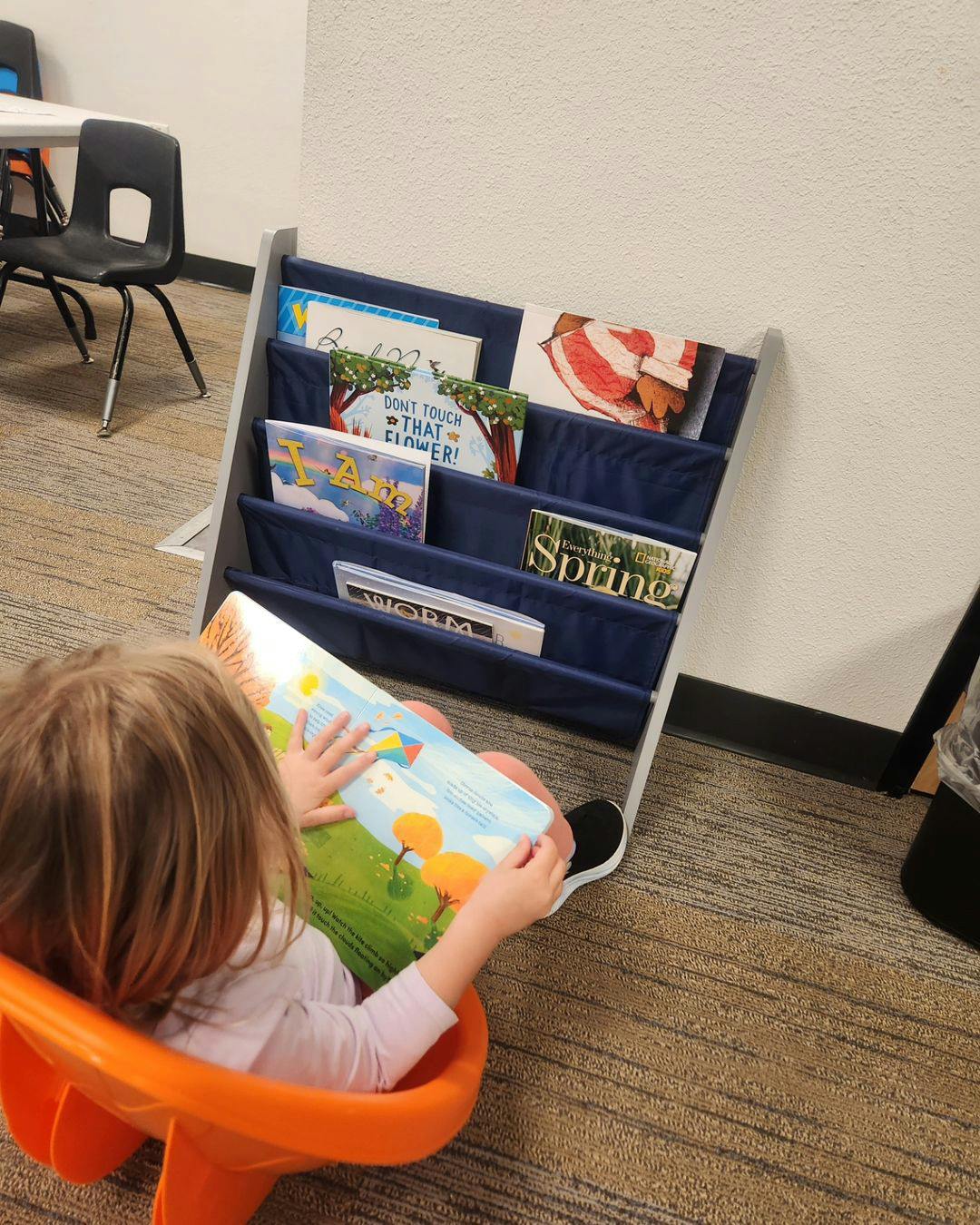 Child sitting in orange chair reading a book next to a bookshelf