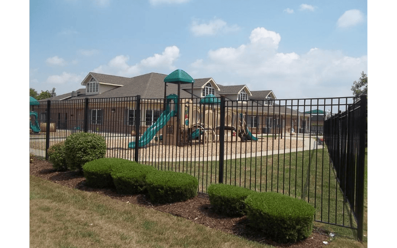 Playground with slides and structures behind a black fence and bushes