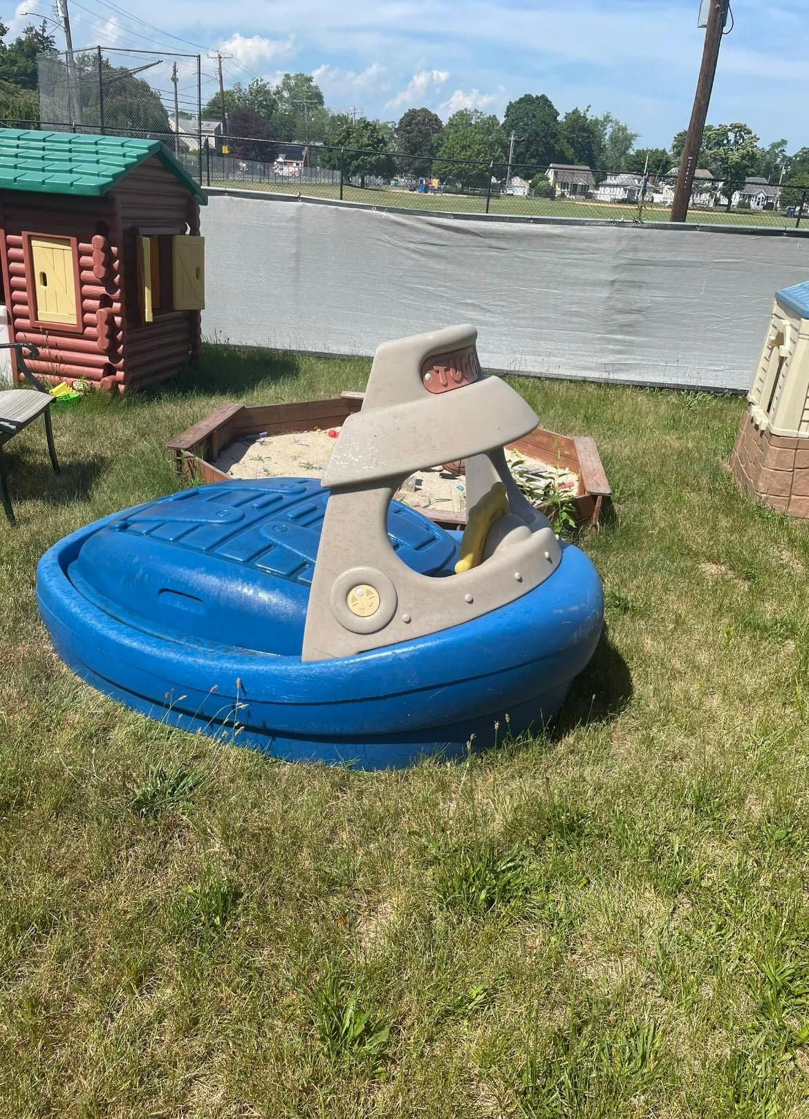 Blue and gray plastic boat-shaped sandbox with a wooden playhouse nearby