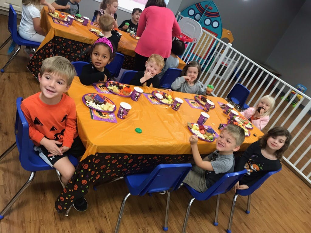 Children sitting at a table with orange tablecloths and Halloween decorations