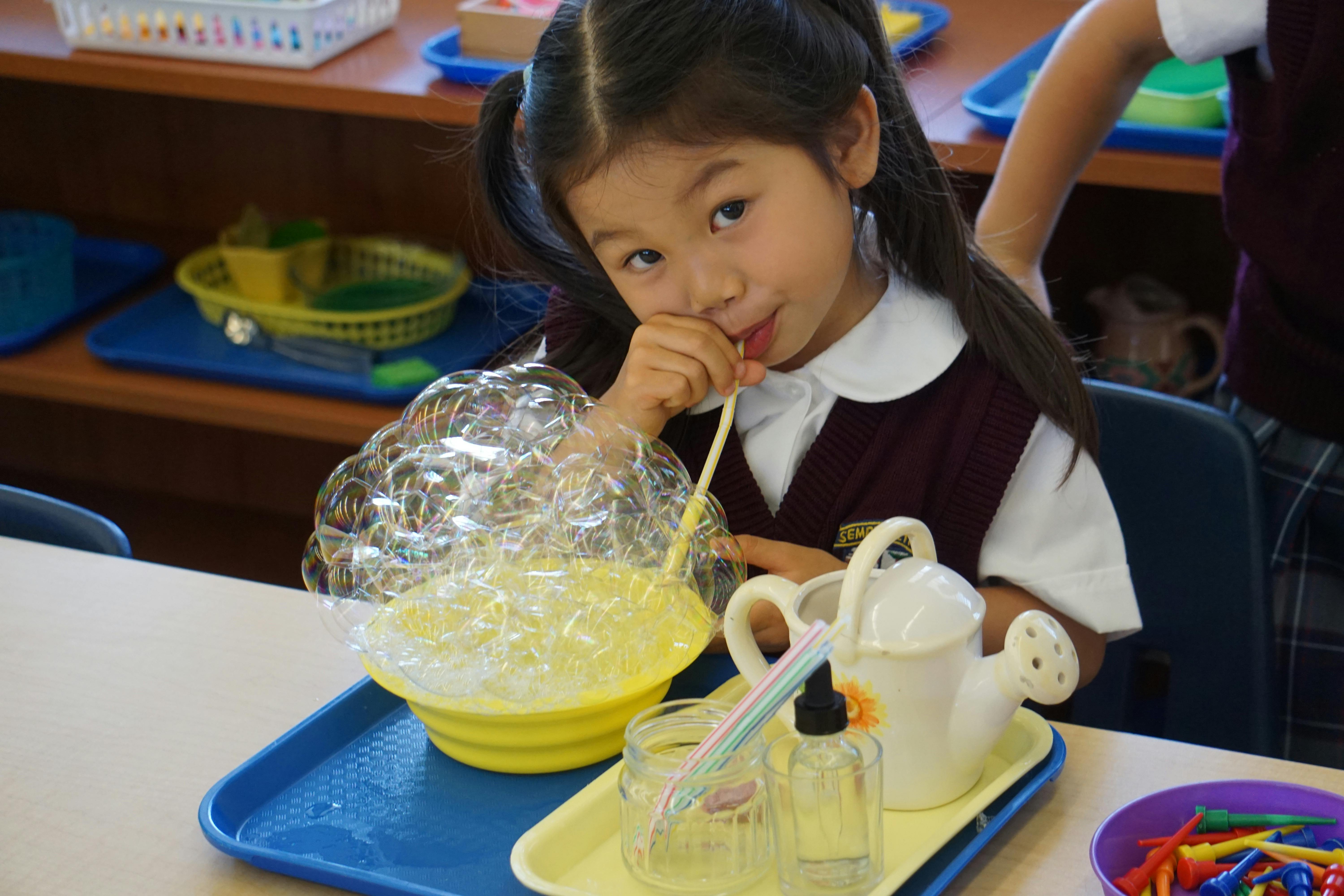 Child blowing bubbles with a straw into a yellow bowl