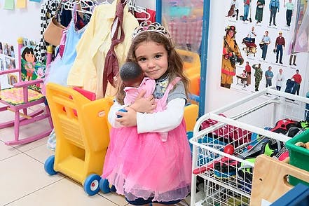 Child wearing a tiara and pink dress holding a doll