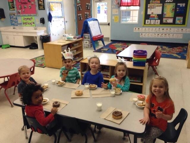 Children sitting at a table with donuts and milk in a classroom