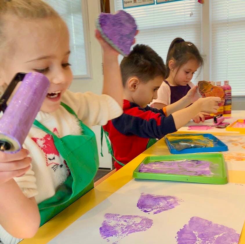 Children painting with purple paint in a classroom