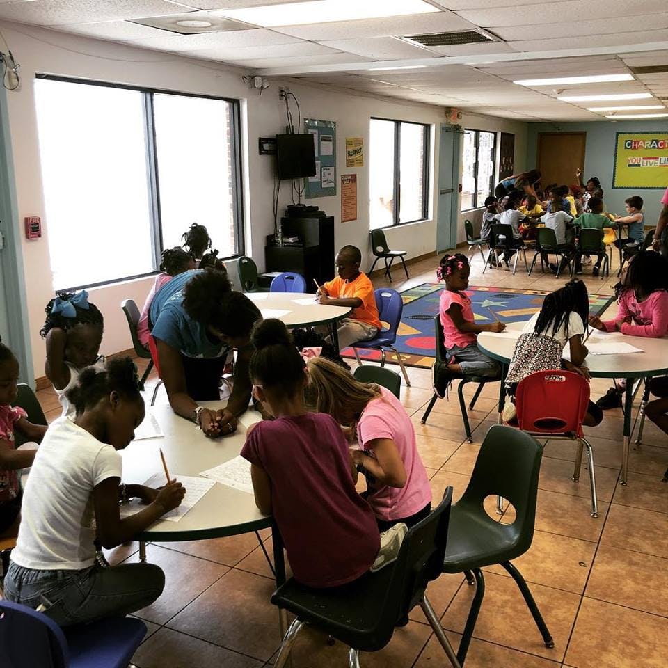 Adult helping children at tables in a classroom