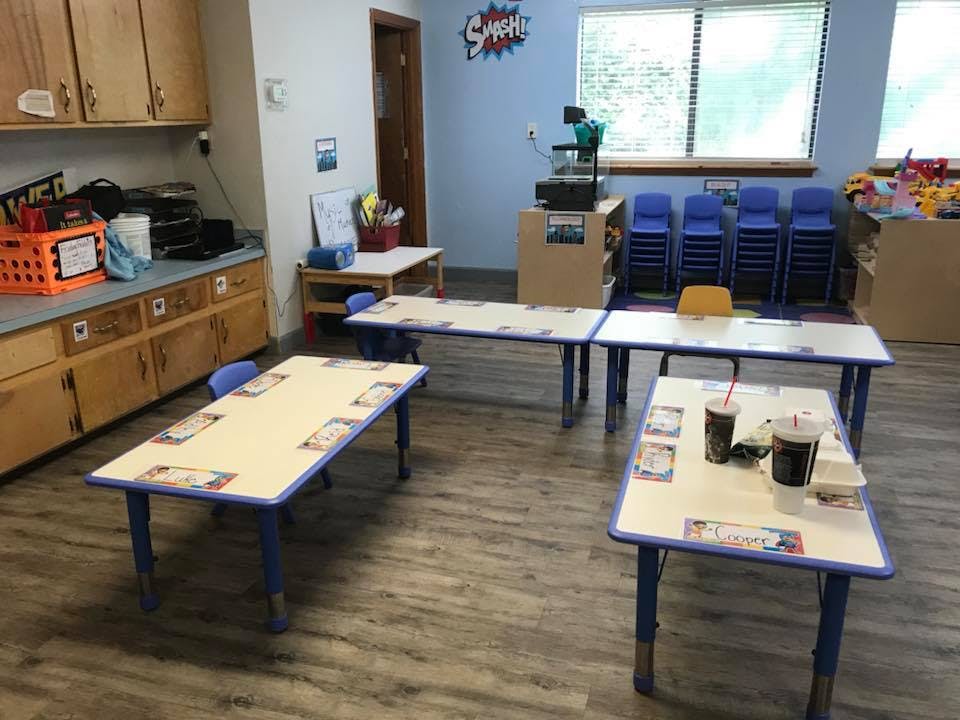 Classroom with multiple tables and chairs, some drinks on a table