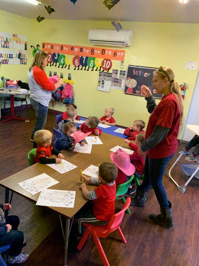 Two adults supervising children coloring at tables in a classroom