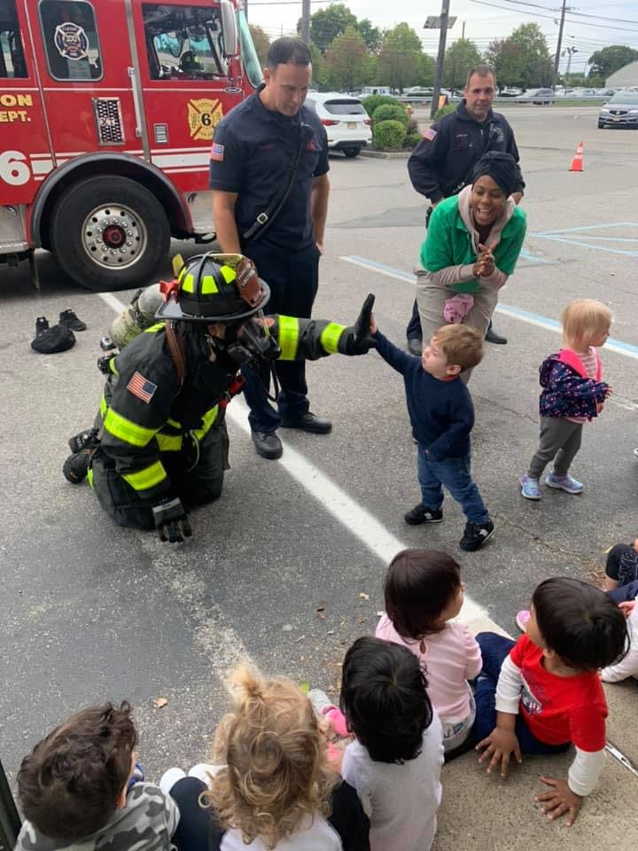 Firefighter in full gear giving a high five to a child, other children watching