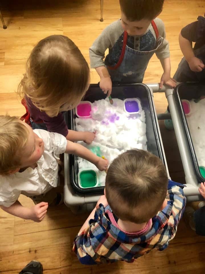 Children playing with sensory bins filled with white material and colored liquids