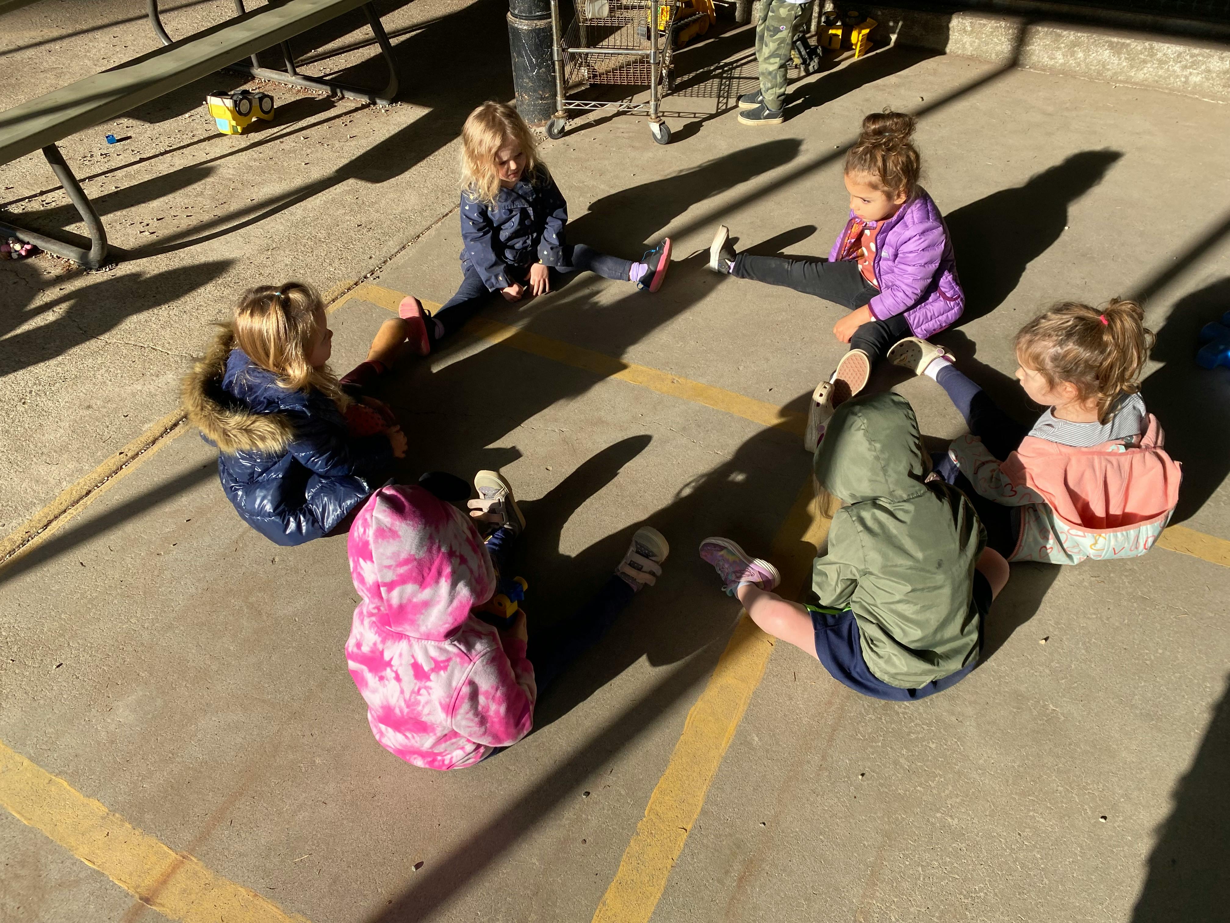 Five children sitting in a circle on pavement