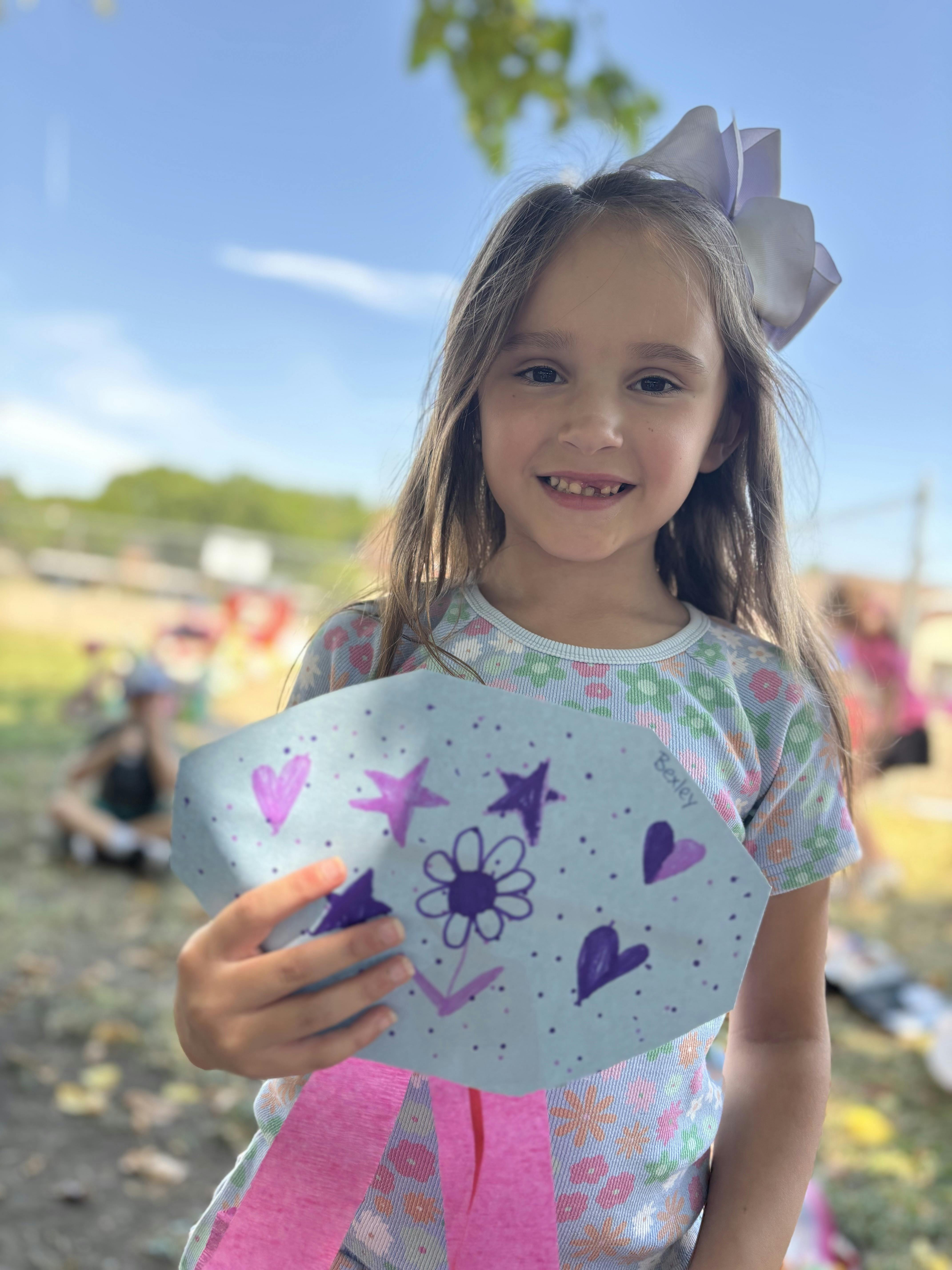 Child holding a paper cutout decorated with drawings of a flower and hearts