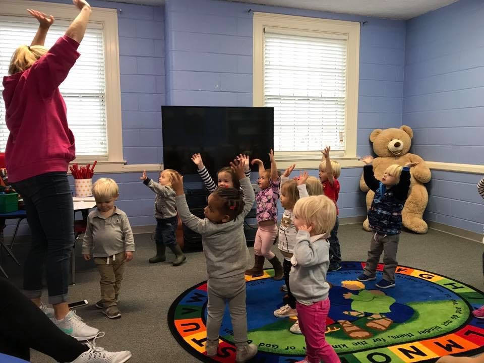 Adult and children with arms raised in a classroom