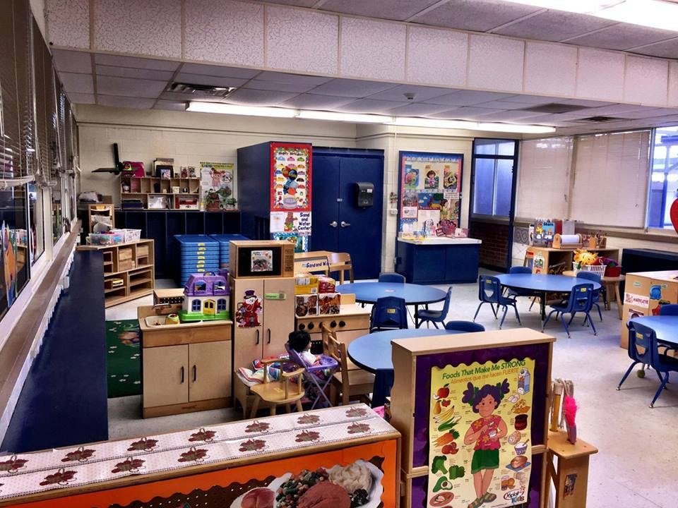 Empty classroom with small tables and chairs, play kitchen, and shelves