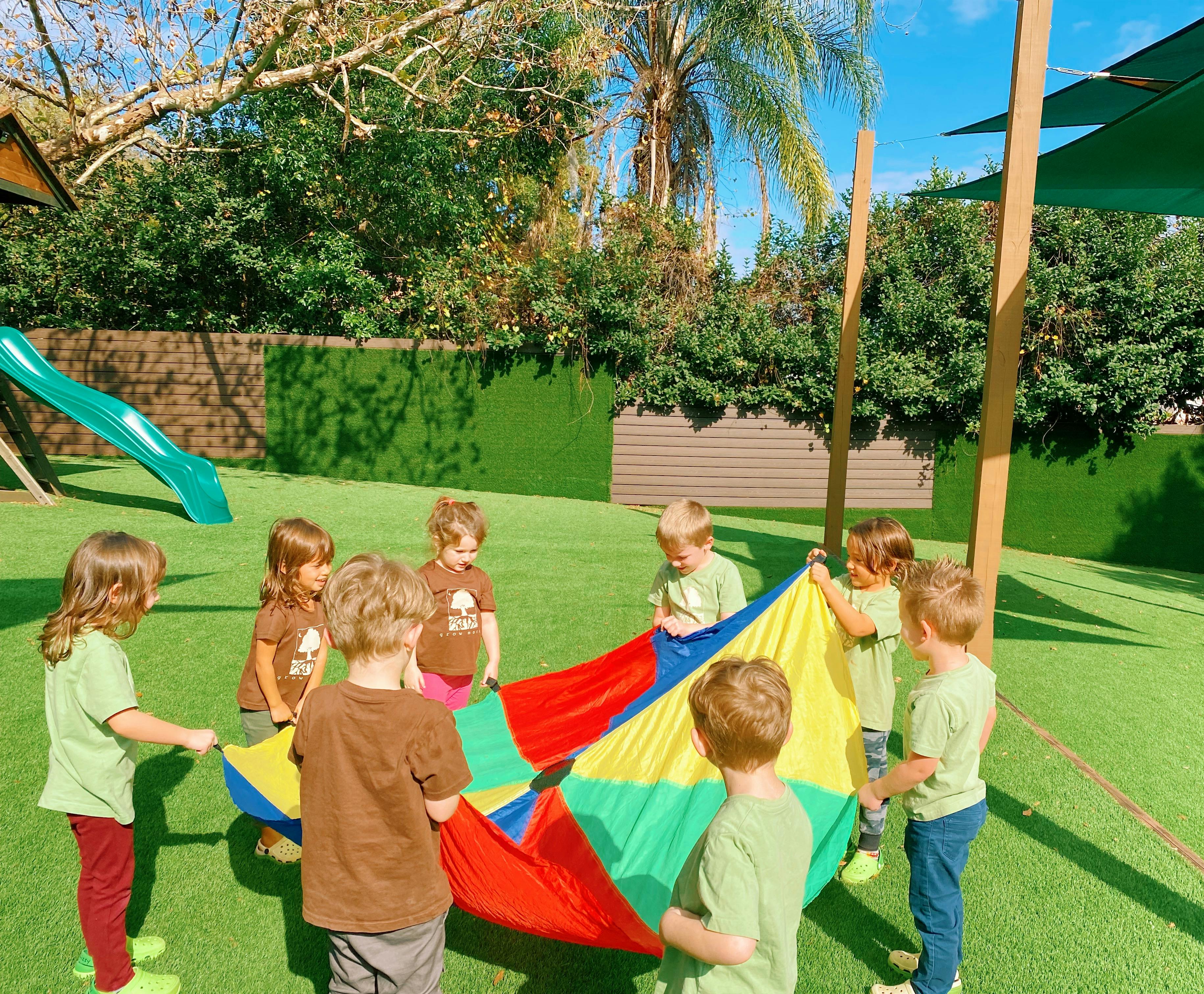 Children playing with a colorful parachute on a grassy playground