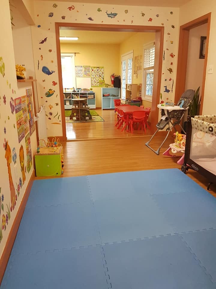 Childcare room with blue floor mats and a view into another room with red tables