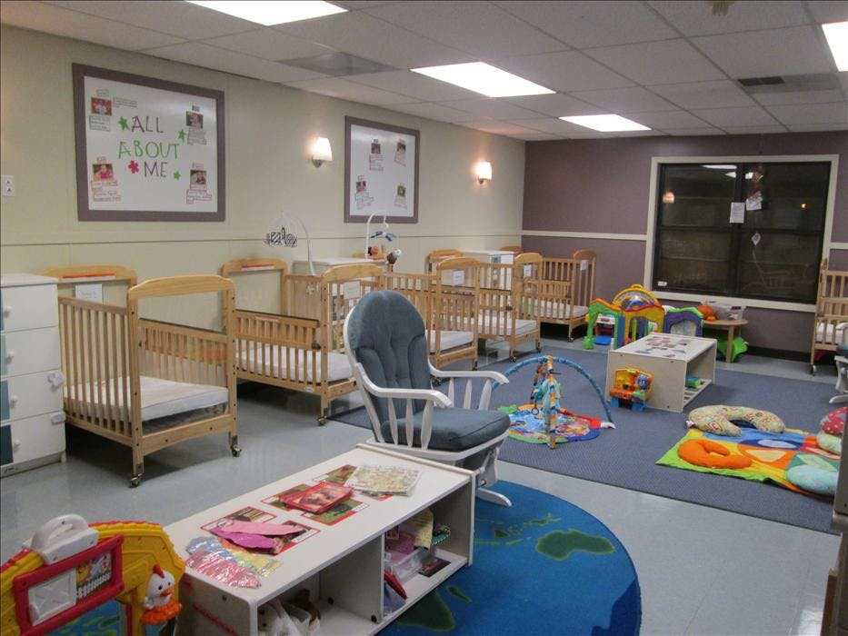 A room with several cribs, a rocking chair, toys, and an "ALL ABOUT ME" poster