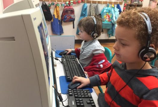 Two children wearing headphones using computers