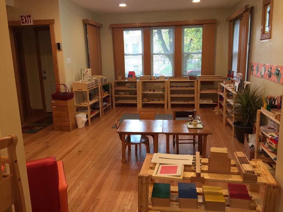 Classroom with wooden tables, chairs, and shelves with learning materials