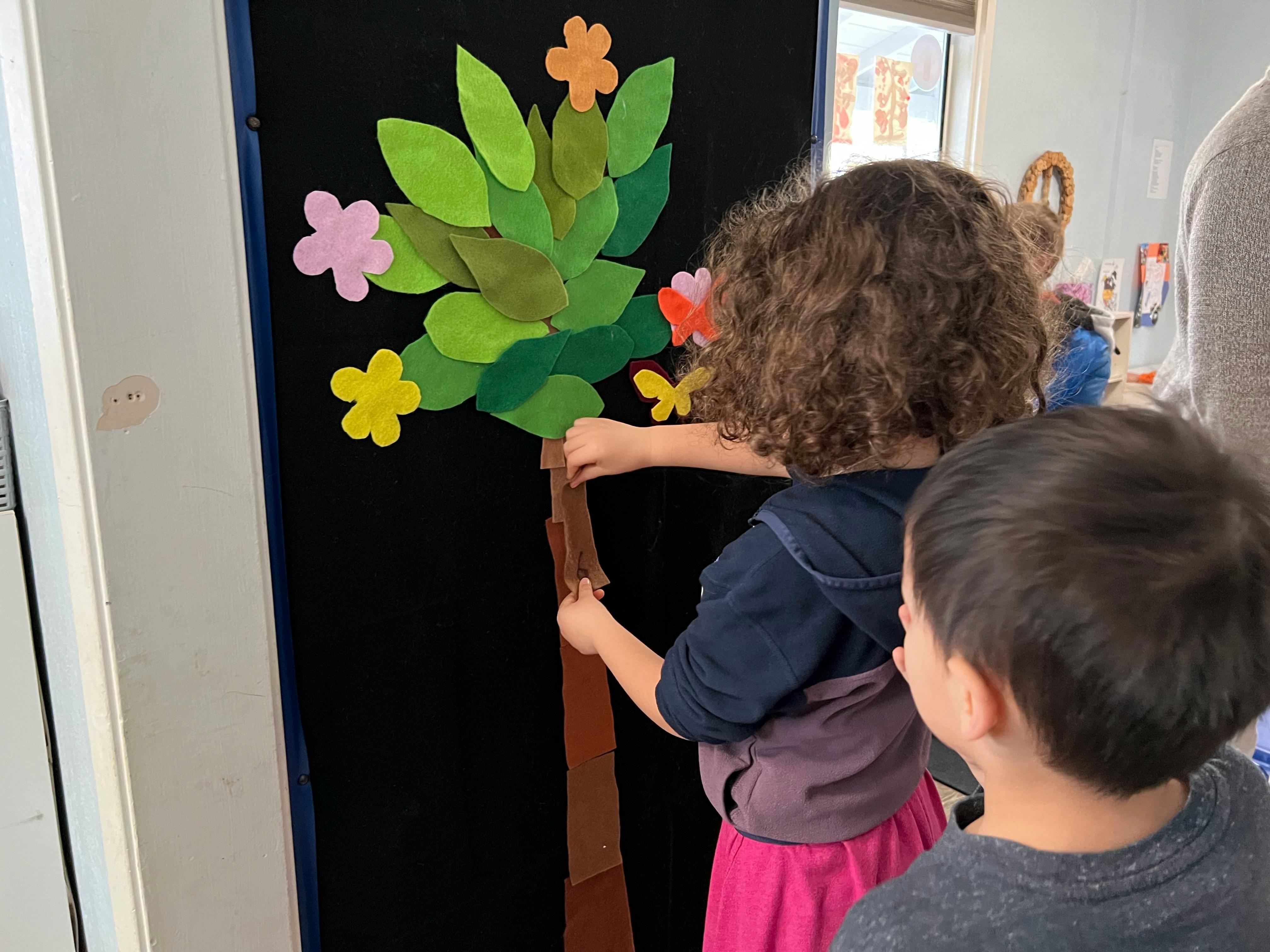 Child placing a felt tree trunk on a black board