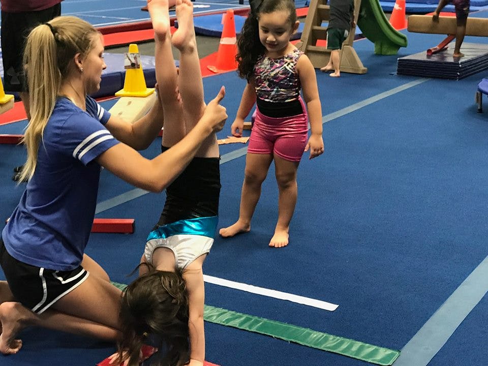Person helping a child do a handstand in a gym