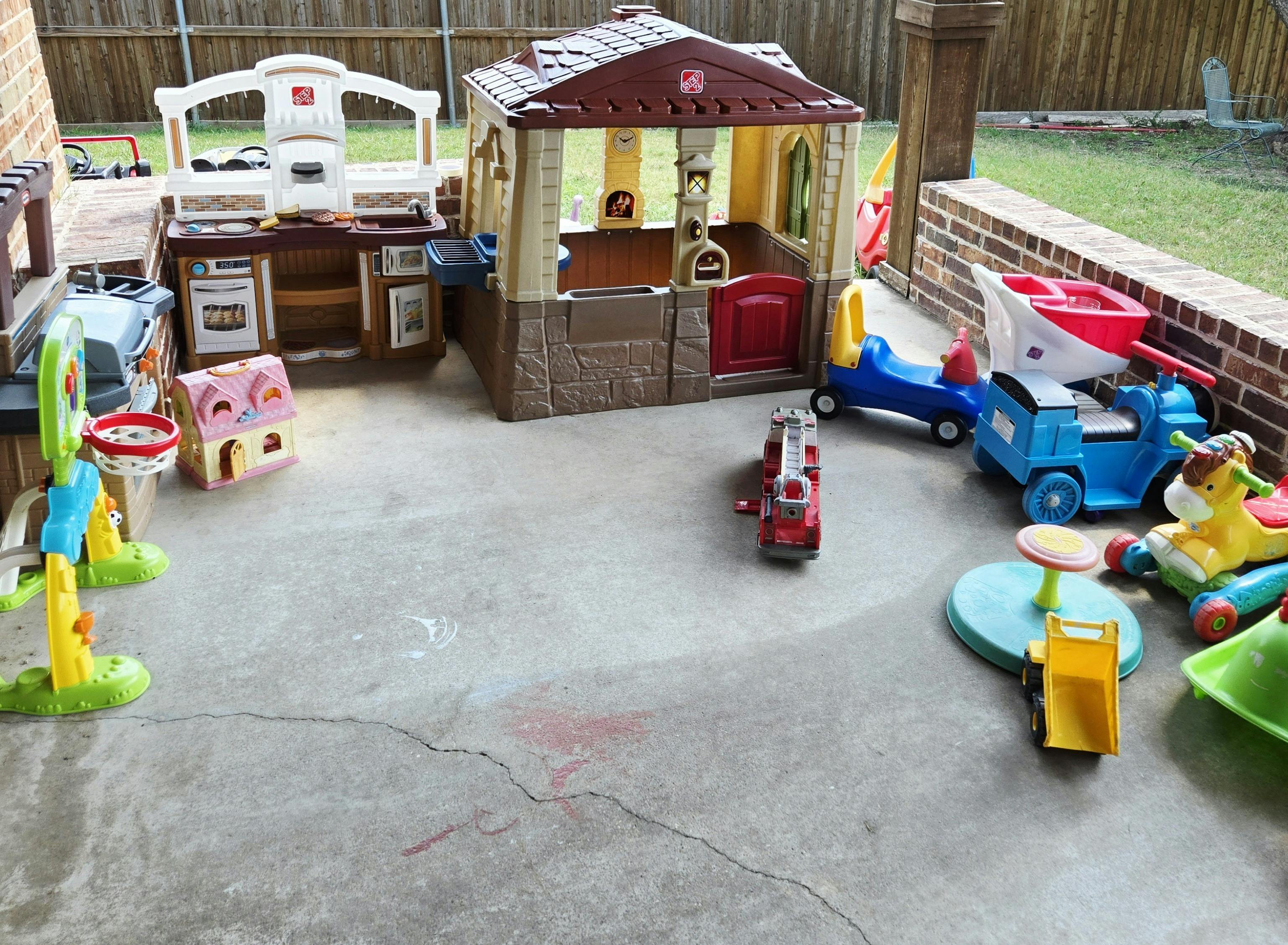 Outdoor play area with a playhouse, toy kitchen, and ride-on toys