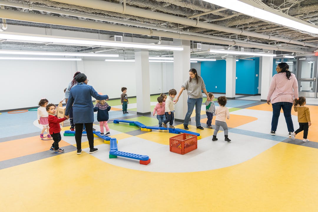 Adults and children in a large room with colorful floor tiles and patterned flooring
