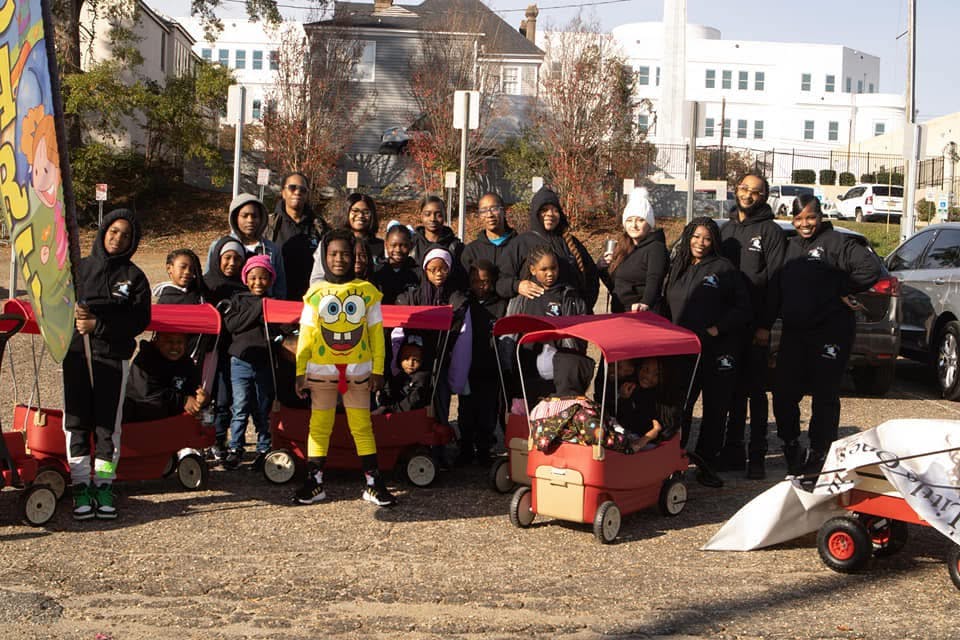 Group of people and children with red wagons, one child in a Spongebob costume