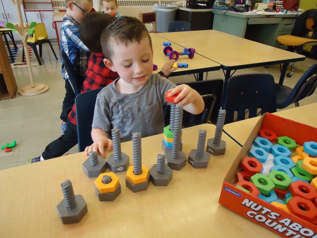 Child playing with large nuts and bolts on a table