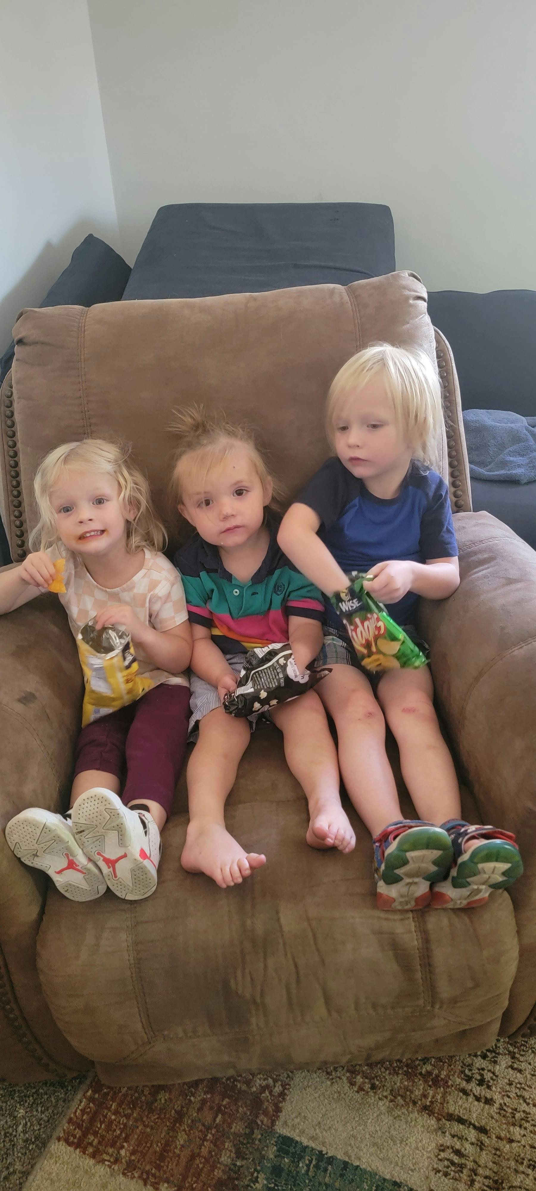Three children sitting on a brown armchair