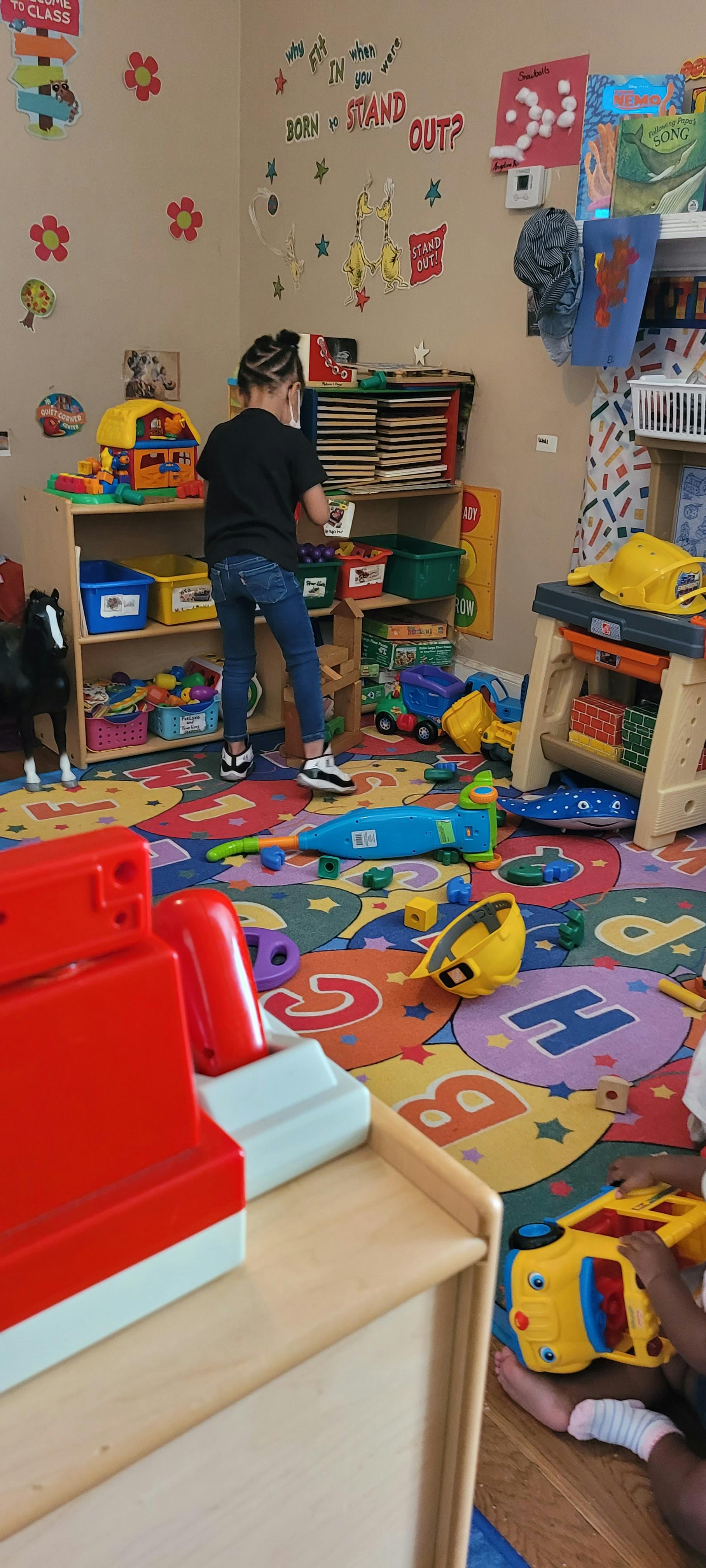 Child standing in a classroom, reaching for items on a shelf