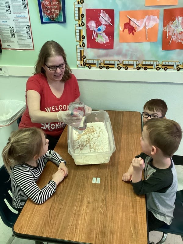 Adult pouring liquid into a container of flour with three children watching