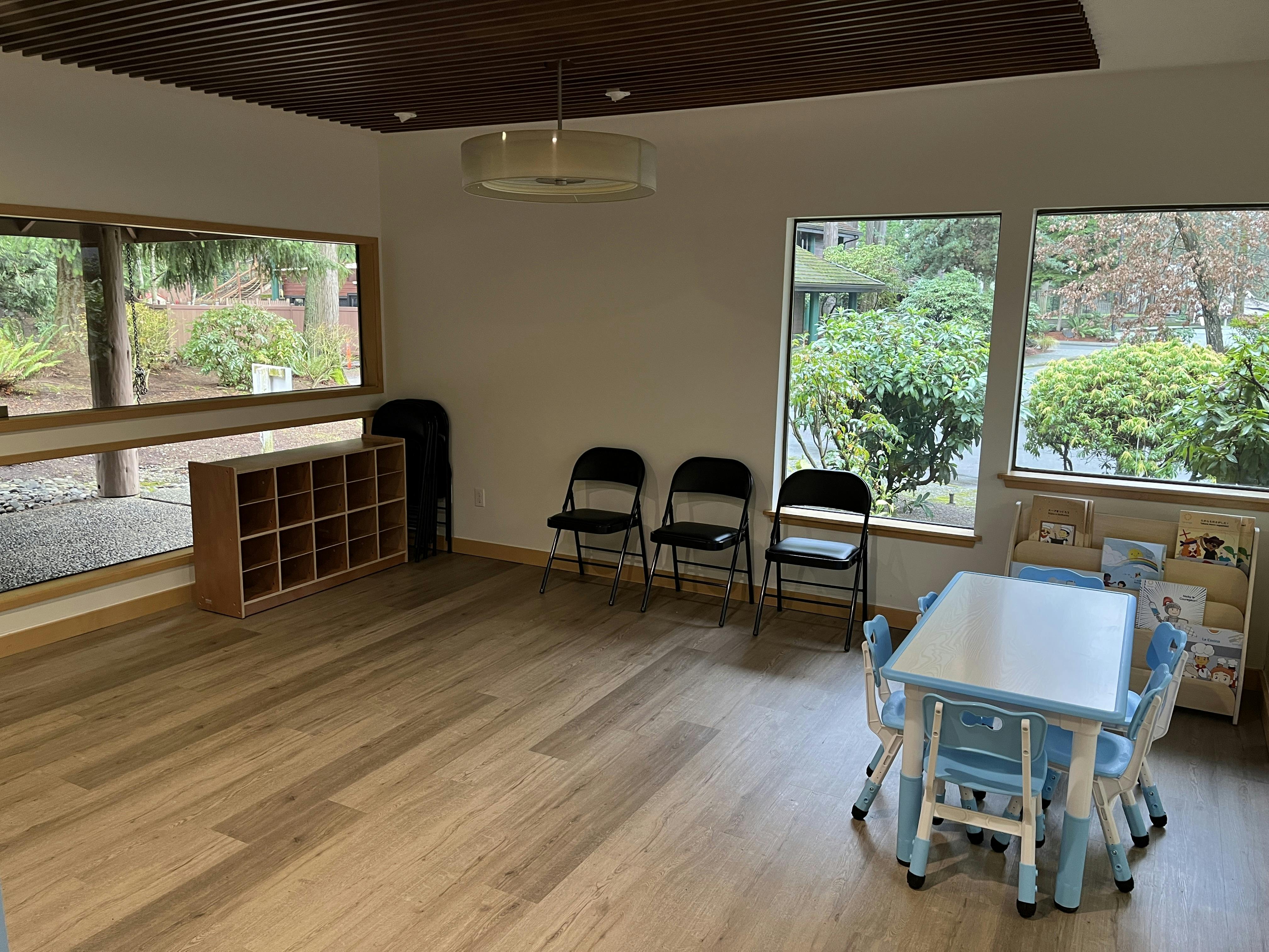 A room with large windows, black folding chairs, and a small table with blue chairs
