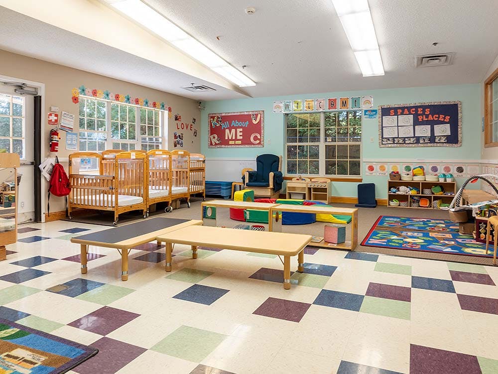 Classroom with cribs, small tables, and shelves with toys