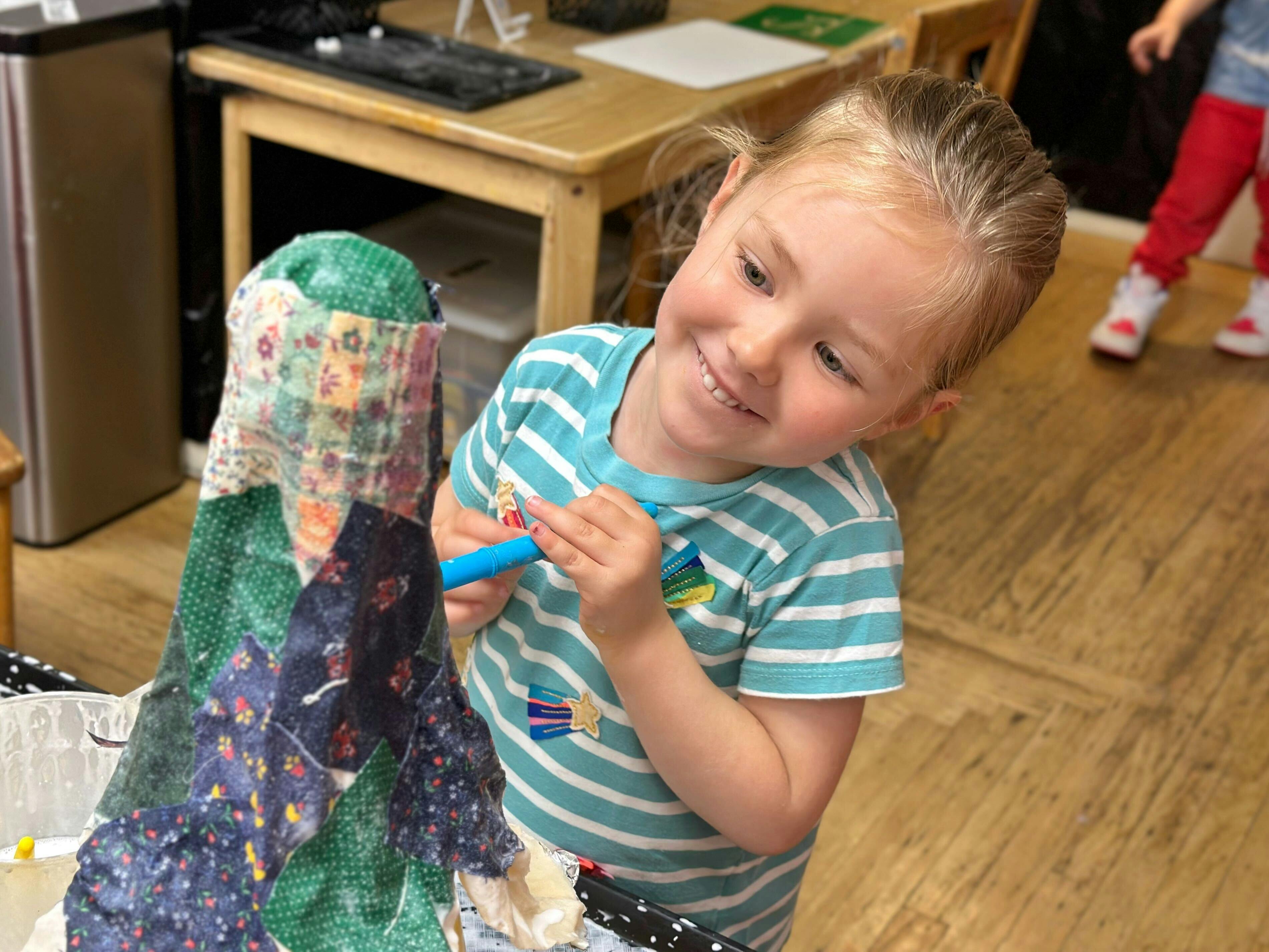 Child holding a blue marker next to a craft project