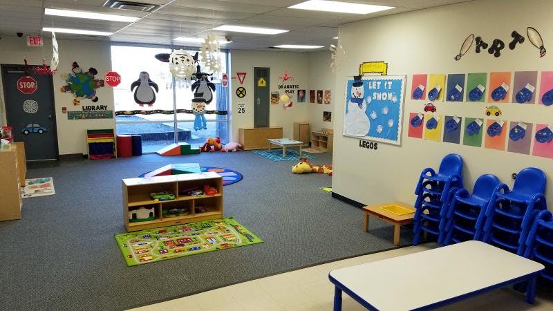 Empty classroom with small tables, chairs, and children's artwork on the wall