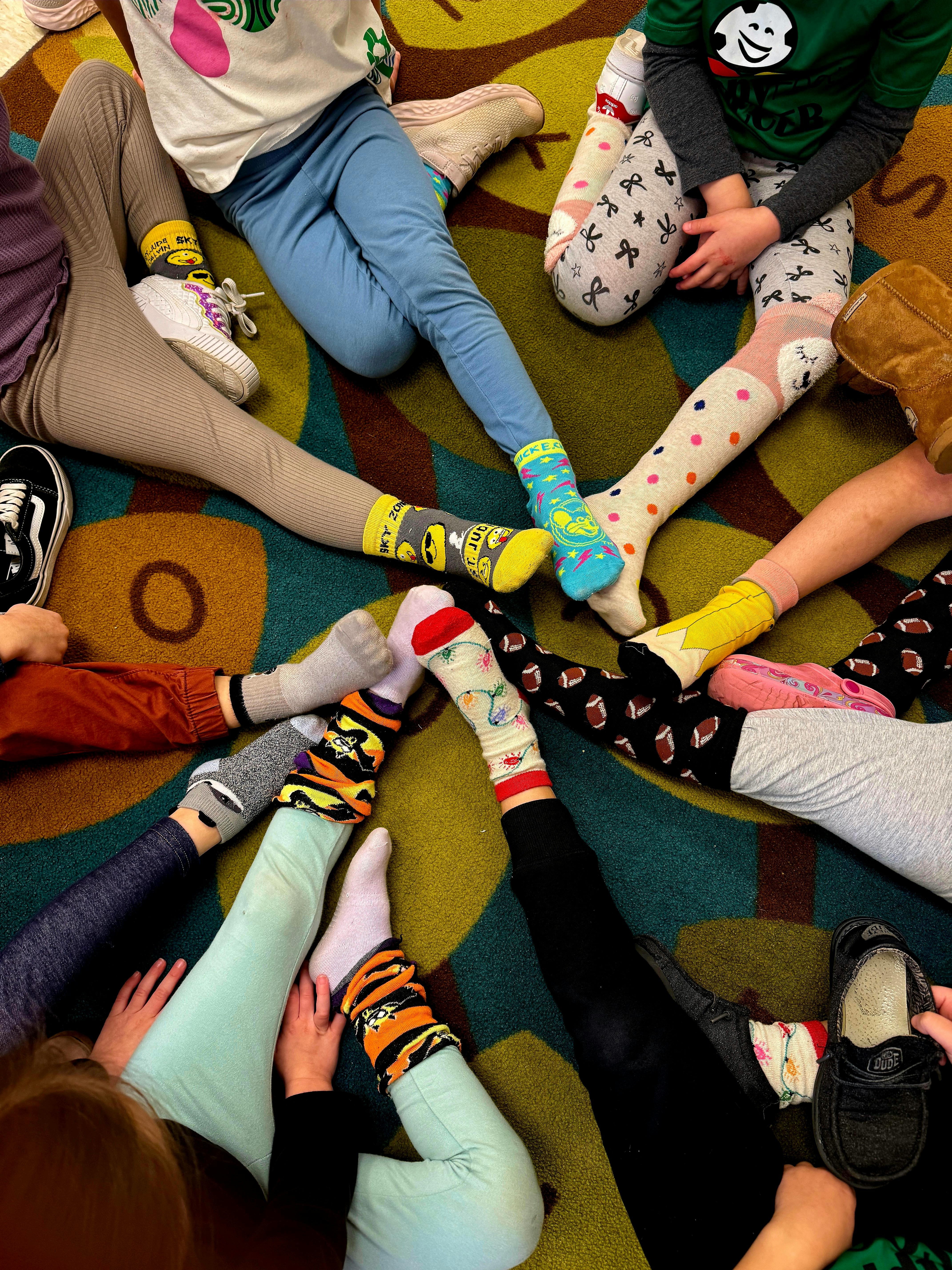 Group of people sitting on a colorful carpet, showing only their legs and feet in various socks