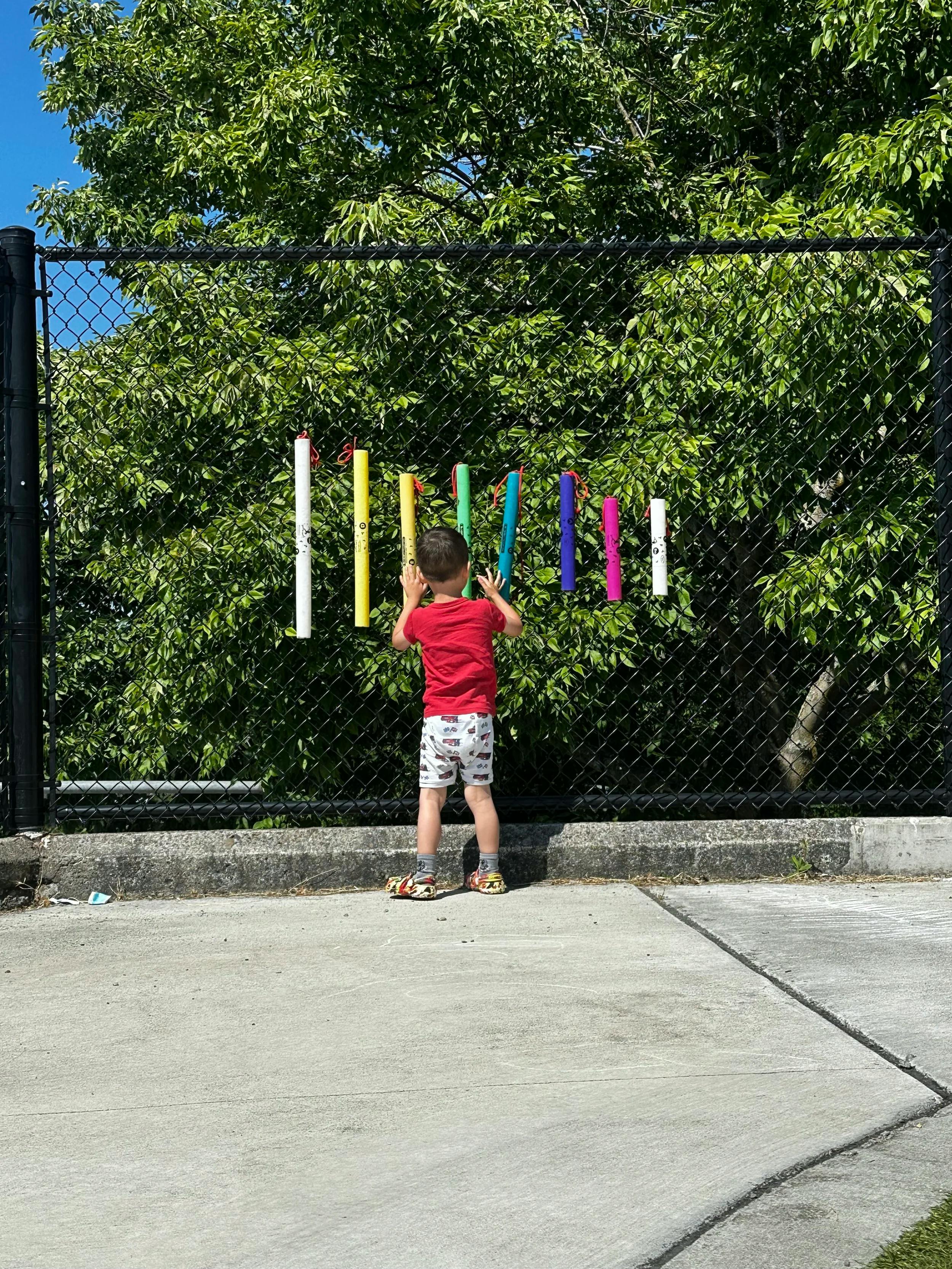 Child facing a fence with colorful foam noodles attached