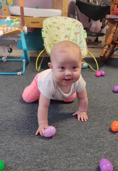 Child crawling on a carpeted floor with colorful plastic eggs