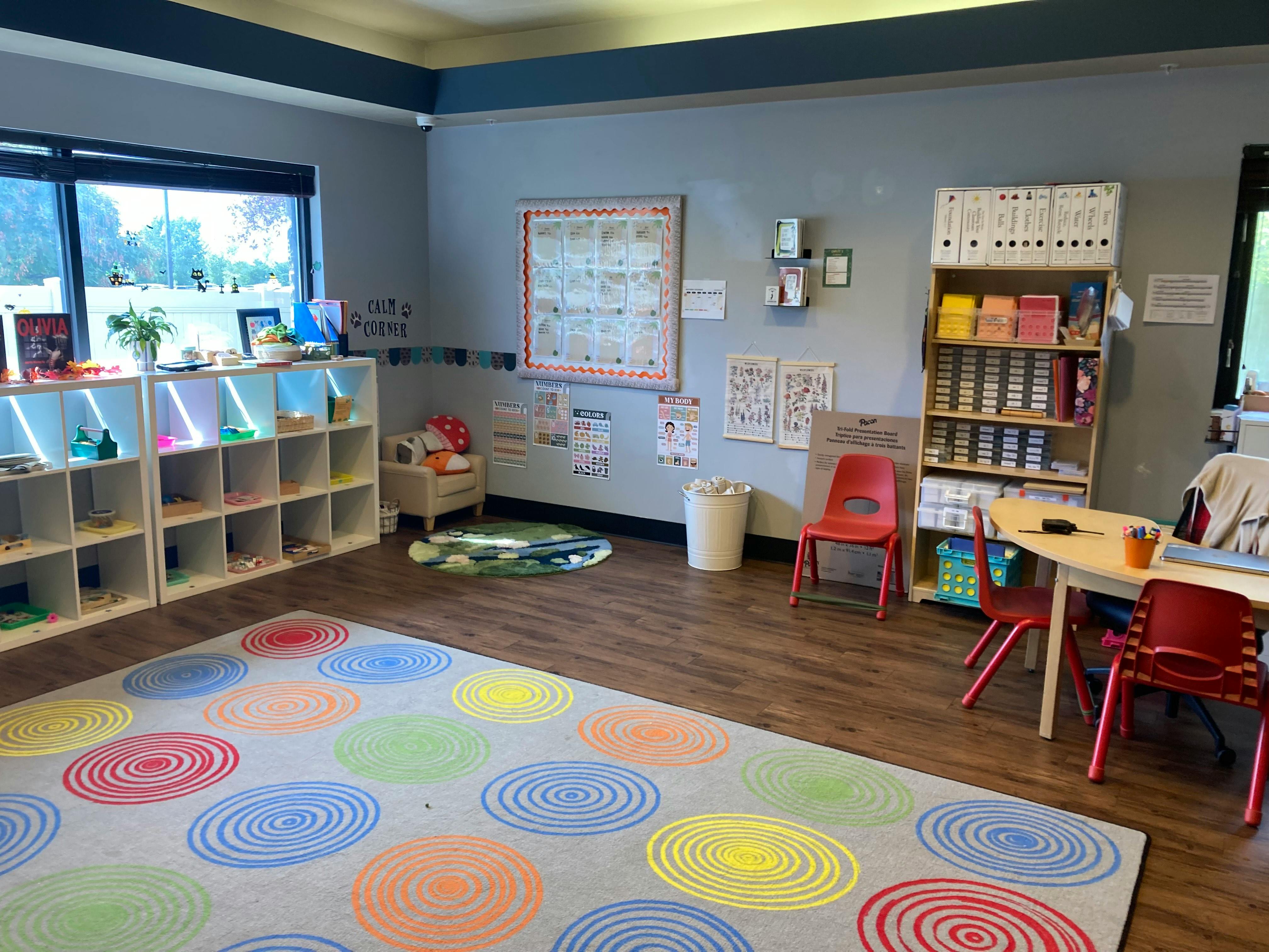 Classroom with colorful rug, shelves, and small tables